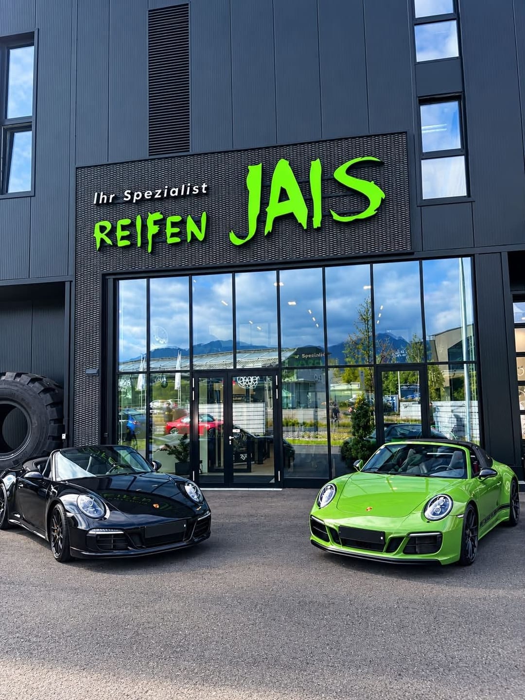 Grüner Schriftzug „Reifen JAIS“ an der Fassade, davor zwei Sportwagen.