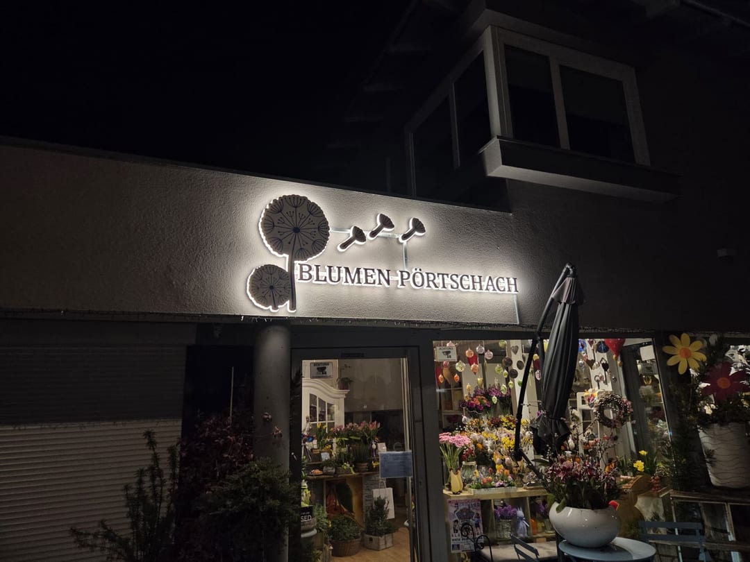 Rückleuchtender Schriftzug „Blumen Pörtschach“ mit Logo bei Nacht.