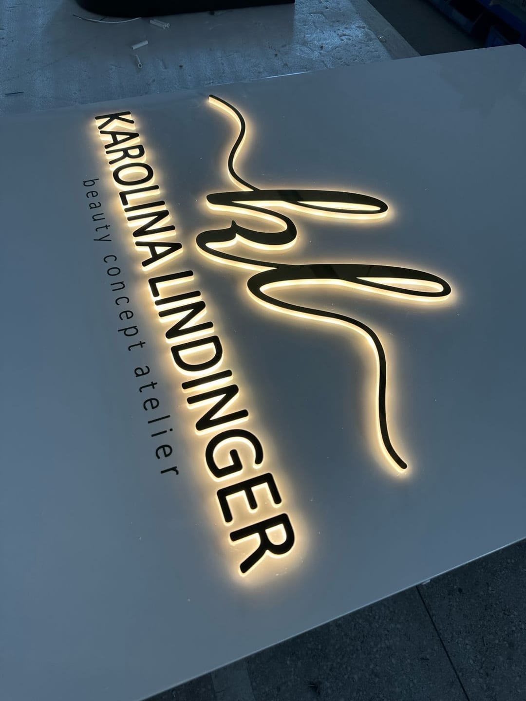 Schwarze Buchstaben und Logo „Karolina Lindinger beauty concept atelier“ mit Lichtsaum.