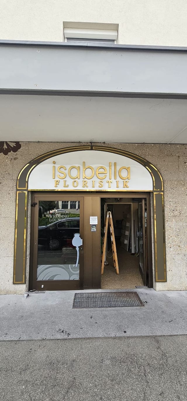 Goldene Buchstaben „isabella FLORISTIK“ auf weißer Fläche im Torbogen über dem Ladeneingang.